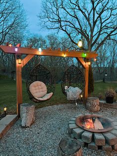 an outdoor fire pit with two hanging chairs next to it and lights on the trees