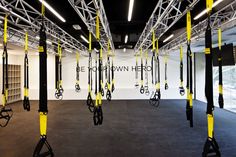 an empty gym room with yellow and black ropes hanging from the ceiling, in front of a white wall