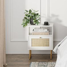 a white nightstand with books and a potted plant on it next to a bed