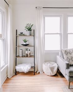 a living room with white walls and wooden floors is pictured in this image, there are plants on the windows sill