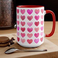 a red and white coffee mug sitting on top of a wooden table next to a cookie