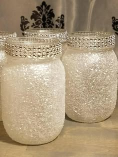 three glass jars with silver glitter on them sitting on a wooden table next to a black and white wall