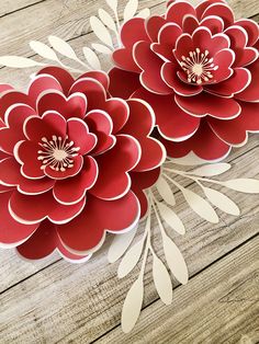 two red paper flowers sitting on top of a wooden table