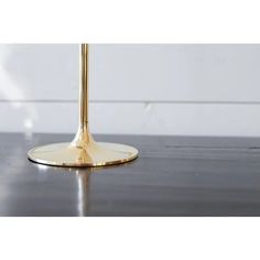 a close up of a gold colored table lamp on a wood floor with white walls in the background