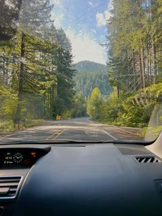 the dashboard of a car on a road with trees and mountains in the back ground