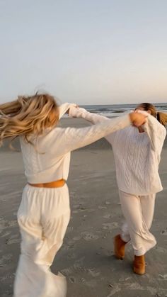 two women are dancing on the beach at sunset, one is holding her hair back