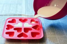 someone is pouring milk into a heart shaped ice cube tray with hearts cut out of it