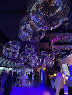 people are standing around in a room with large bubbles hanging from the ceiling and lights on the walls