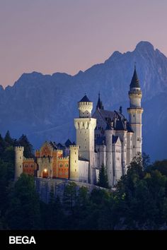 an old castle sits on top of a hill with mountains in the background at dusk