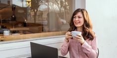 a woman sitting at a table with a laptop and holding a cup