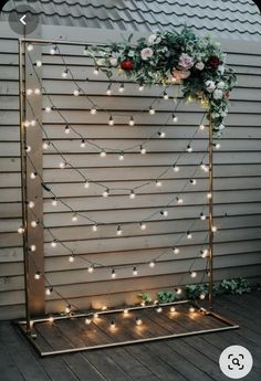 a wedding arch decorated with flowers and greenery is lit up by fairy lights on the side