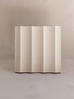 a white sculpture sitting on top of a gray floor next to a wall with vertical lines