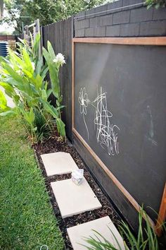 a blackboard with writing on it next to a small flower bed in the grass