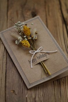 a birthday card with dried flowers tied to it on top of a wooden table,