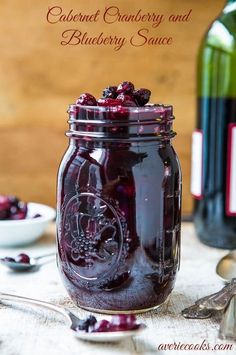 two jars filled with cranberry sauce next to spoons and bottles of wine