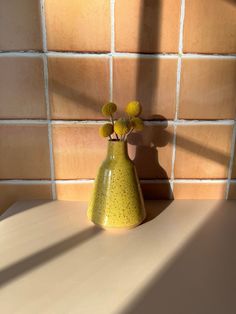 a yellow vase sitting on top of a counter next to a wall covered in tiles