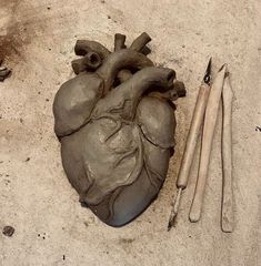 a heart shaped clay sculpture next to some tools on the ground with sand in front of it