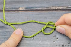 someone is tying a green string to a piece of wood with one hand and two fingers