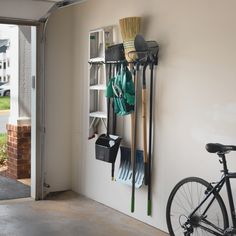 a bike is parked next to a wall mounted rack with brooms and rakes