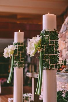 two tall white candles are decorated with greenery and flowers