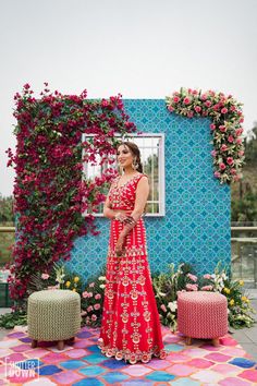 a woman standing in front of a colorful wall with flowers on it and an open window