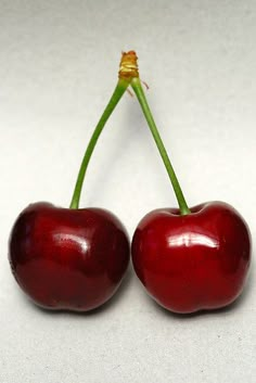 two cherries sitting next to each other on a white surface