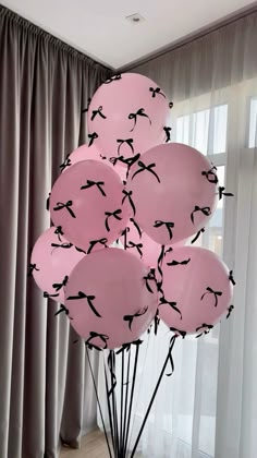 a bunch of pink balloons with black birds on them in front of a curtained window