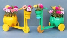 three colorful flower pots sitting on wheels with flowers in the middle one is yellow and the other two are green