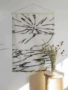 a vase with some flowers in it next to a wall hanging on a white wall