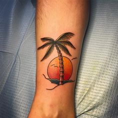 a small palm tree tattoo on the arm and foot with an orange sunset behind it