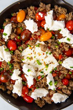 a skillet filled with meat, tomatoes and feta cheese on top of a table