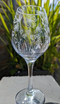 a clear wine glass sitting on top of a table next to some grass and flowers