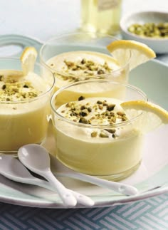 three desserts on a plate with spoons and lemon slices in the bowl next to them