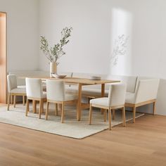 a dining room table with chairs and a vase on it's centerpiece in front of a white wall