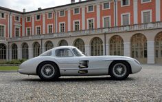 an old silver sports car is parked in front of a large building with arched windows