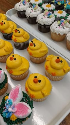 cupcakes with yellow frosting decorated as easter eggs and bunny ears are on display