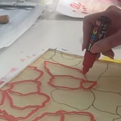 a person is using glue to decorate a piece of paper with red lines on it