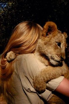 a woman holding a baby lion in her arms