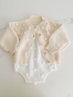 Soft and cozy, this stunning knit cardigan is the perfect addition to your little ones closet. Tiny Pom Pom appliqués all over. Textured pattern with front buttons. Cute Soft Knit Outerwear For Fall, Cute Cotton Cable Knit Sweater, Cute Soft Knit Fall Outerwear, Playful Knit Long Sleeve Outerwear, Cute Cream Soft Knit Sweater, Cute Cream Cotton Cardigan, Playful Knit Cardigan For Winter, Playful Long Sleeve Knit Cardigan, Cute Long Sleeve Knit Cardigan