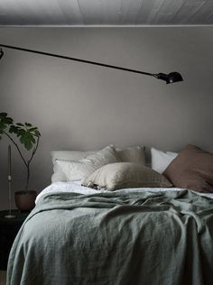 a bed sitting under a lamp next to a green plant in a room with gray walls