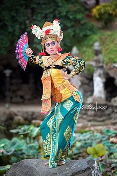 a woman dressed in traditional thai garb holding an umbrella and standing on a rock