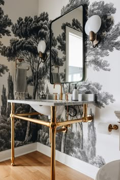 a bathroom with wallpaper and a mirror above the sink that has gold faucets on it