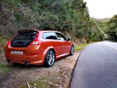 an orange car parked on the side of a road next to a wooded area with trees