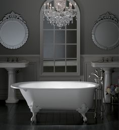 a white bath tub sitting under a chandelier next to two sinks in a bathroom