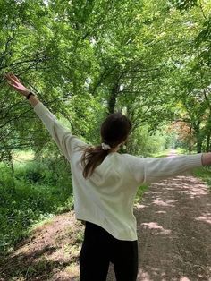 a woman standing in the middle of a forest holding her arms out with both hands