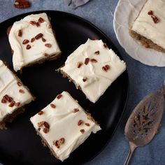 four pieces of cake on a black plate next to a silver spoon and two plates with pecans