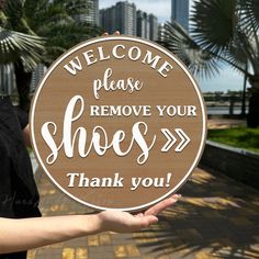 a woman holding up a sign that says, welcome please remove your shoes thank you