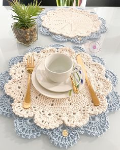 two crocheted placemats and a cup on a white table with silverware