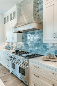 a kitchen with white cabinets and blue glass backsplash tiles on the stove top