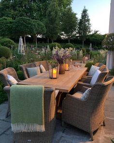 a wooden table surrounded by wicker chairs with candles on it and flowers in vases